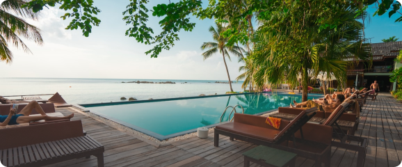 Piscine avec vue sur la mer, entourée de transats, de palmiers et d’une terrasse en bois.